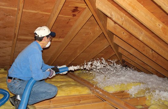 Technician installing blown-in white fiberglass insulation in an attic.