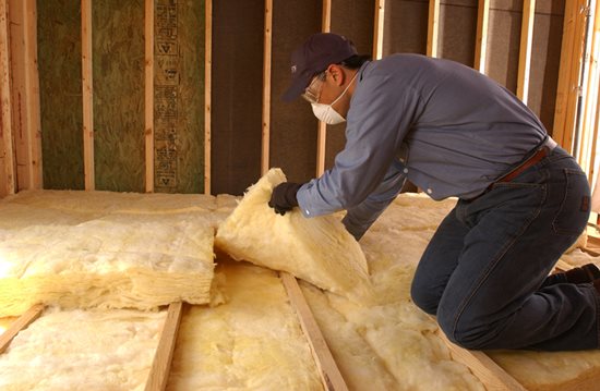 Technician installing yellow/white batt fiberglass insulation in an attic floor.