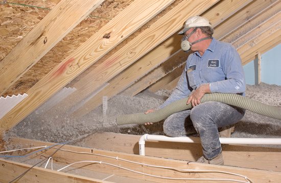 Technician installing gray blown-in loose-fill cellulose insulation in an attic.